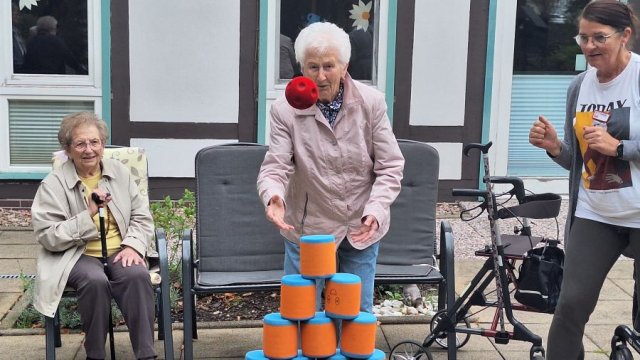 Das Bild zeigt eine Frau, die einen roten Ball auf eine Pyramide aus Schaumstoffquadern wirft.
