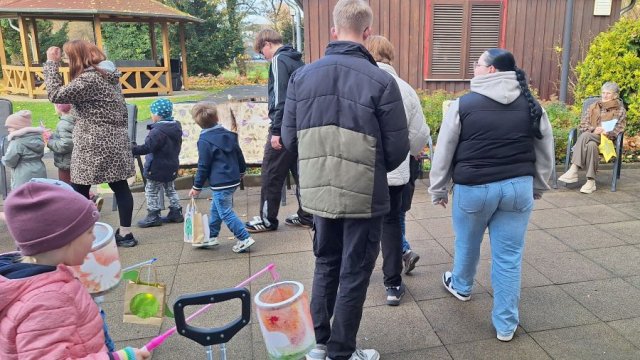 Das Foto zeigt Kinder, die mit ihren Laternen einen kleinen Umzug veranstalten, begleitet von Erwachsenen.