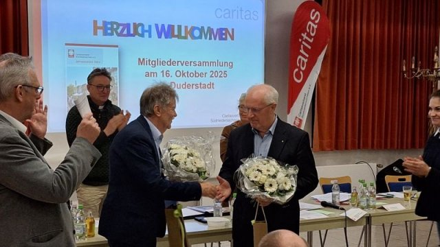 Das Bild zeigt applaudierende Menschen. In der Mitte verabschieden sich Bernward Jacobi und Alfons Wüstefeld aus dem Caritasrat.